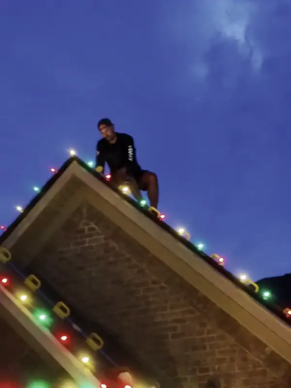 A Hisway Lighting crew member on the ridge at dusk, clipping a lit C7 strand in place